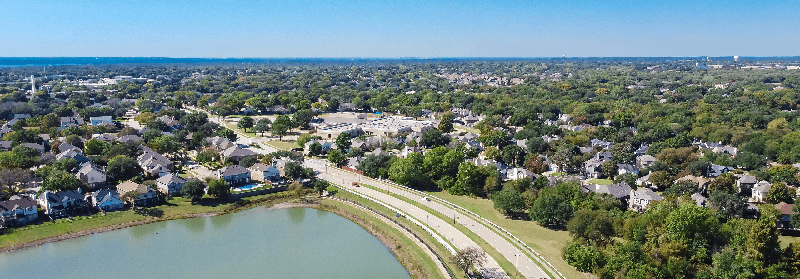 Aerial view residential neighborhood with Grapevine Lake in horizontal line. Row of upscale two story suburban residential houses near local pond in Flower Mound, Texas, America